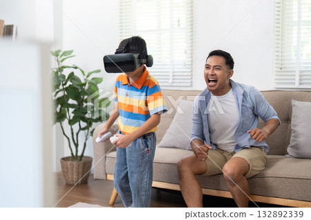 Excitement and Virtual Reality. A father cheers as his son plays a VR game at home. Excitement and Virtual Reality. A father cheers as his son plays a VR game at home. 132892339