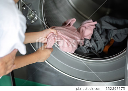 Laundry and Learning. A mother assists her son with loading clothes into the washing machine. 132892375
