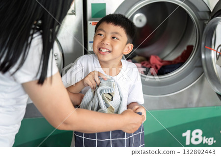 Cleaning and Family Bonding. Child helping mother with laundry at laundromat. 132892443