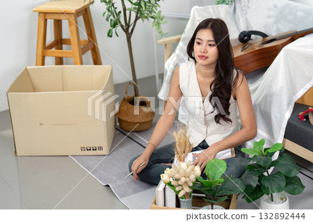 Reflecting in a New Space. A woman sits with plants, contemplating her new home. 132892444