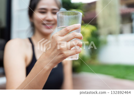 Wellness and Hydration. Young woman enjoying a refreshing glass of water outdoors. Wellness and Hydration. Young woman enjoying a refreshing glass of water outdoors. 132892464