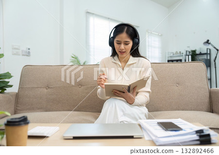 Focused Study Session. Woman in headphones taking notes while using laptop. 132892466