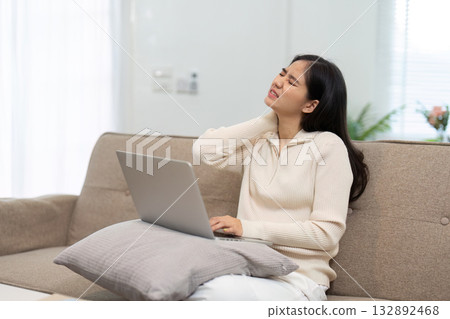 Remote Work and Ergonomics. Young woman experiencing neck pain while using laptop on sofa. 132892468