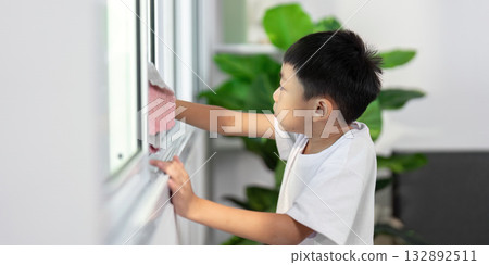 Cleaning and Learning. A young boy cleans a window, learning responsibility and hygiene at home. Cleaning and Learning. A young boy cleans a window, learning responsibility and hygiene at home. 132892511