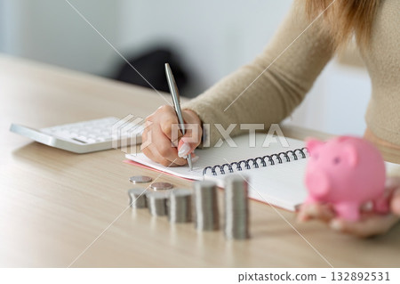 Financial Planning and Budgeting. Woman writing in notebook while managing coins and piggy bank. Financial Planning and Budgeting. Woman writing in notebook while managing coins and piggy bank. 132892531
