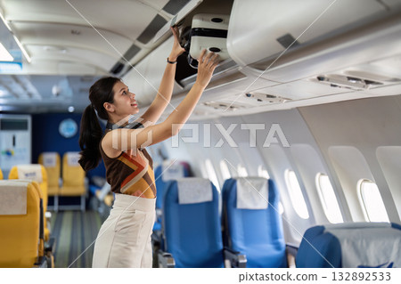 Tourist and Air Travel. A traveler placing luggage in the overhead compartment of an airplane. Tourist and Air Travel. A traveler placing luggage in the overhead compartment of an airplane. 132892533