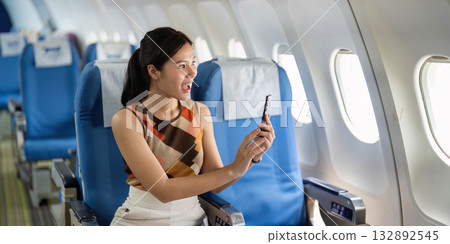 Excited Tourist on Airplane. A young woman joyfully capturing a moment with her phone. Excited Tourist on Airplane. A young woman joyfully capturing a moment with her phone. 132892545