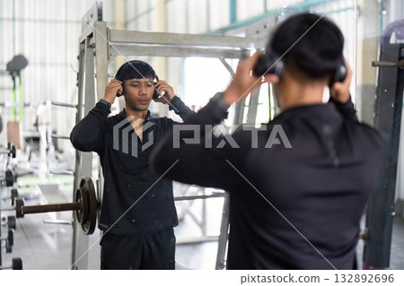 Wellness and Motivation. Young man adjusting headphones before workout in gym. Wellness and Motivation. Young man adjusting headphones before workout in gym. 132892696