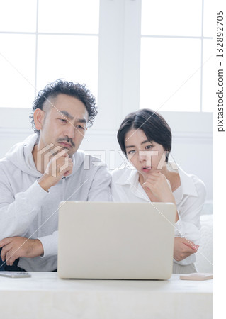 Couple looking at computer in living room, thinking seriously, worrying, wondering, searching and finding, looking for moving, insurance, etc. 132892705