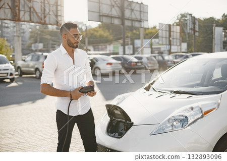 Young adult man charging his electric car in the city. Eco electric car concept. Young adult man charging his electric car in the city. Eco electric car concept. 132893096