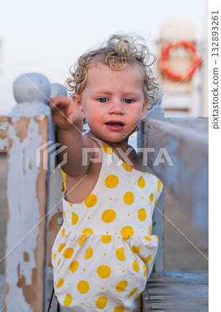 A young girl in a yellow polka dot dress is standing on a wooden fence A young girl in a yellow polka dot dress is standing on a wooden fence 132893261