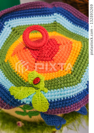 A colorful crocheted hat with a green leaf and a red ladybug on it 132893269