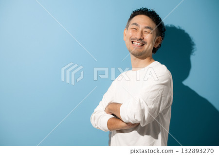 一位留著清爽鬍鬚的中年男子，雙手交叉抱在胸前，在淺藍色背景下看向鏡頭。 132893270