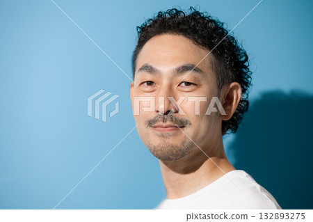 Close-up of a bearded middle-aged man looking at camera against a light blue background Close-up of a bearded middle-aged man looking at camera against a light blue background 132893275