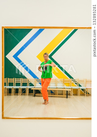 A woman in a green shirt is standing in front of a mirror A woman in a green shirt is standing in front of a mirror 132893281