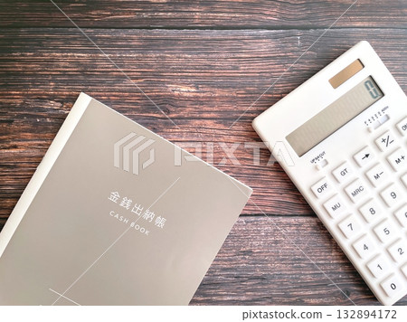 White calculator and household account book on a wooden table White calculator and household account book on a wooden table 132894172