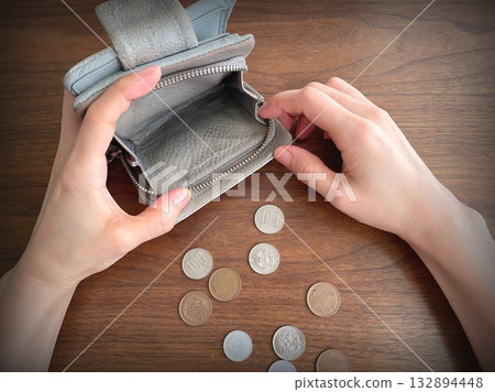 A woman's hand opening an empty wallet and coins on a table 132894448