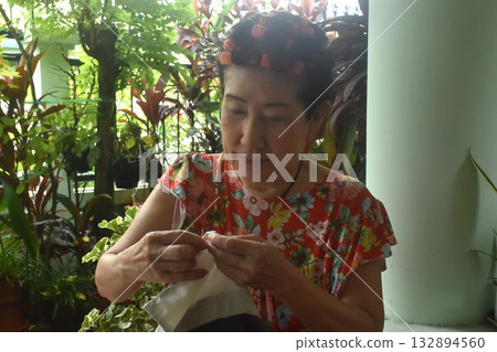 Asain elder woman sewing cloth for repairing in home front yard Asain elder woman sewing cloth for repairing in home front yard 132894560
