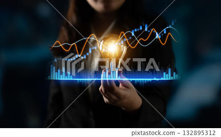 Businesswoman Holding Light Bulb with Economic Graphs and Financial data Visualization in Modern Office Background for Innovation and Strategy Scalp 132895312