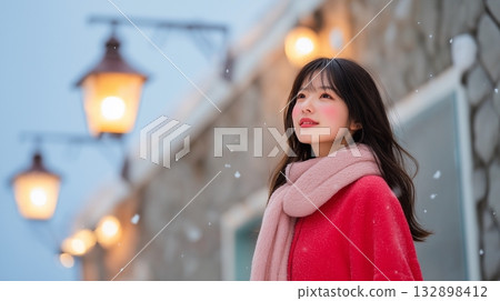 一位女子在燈火通明的街道上抬頭望著白雪皚皚的天空。 132898412