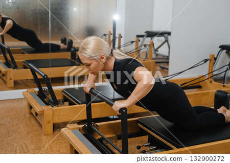 Woman performing exercise on reformer in a bright fitness studio during morning hours to strengthen upper body and improve overall fitness levels Woman performing exercise on reformer in a bright fitness studio during morning hours to strengthen upper body and improve overall fitness levels 132900272