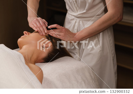 Relaxation and rejuvenation during a facial treatment at a serene spa, showcasing hands gently massaging the client's forehead to relieve tension and promote tranquility 132900332