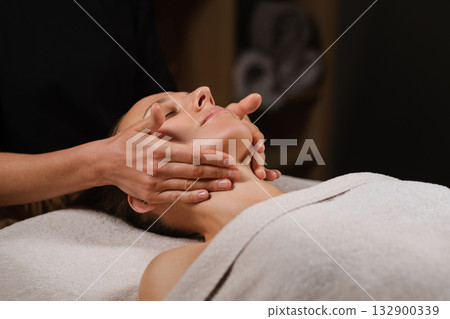 Relaxing facial massage session at a serene wellness spa with calming ambiance and skilled hands working on a client's face Relaxing facial massage session at a serene wellness spa with calming ambiance and skilled hands working on a client's face 132900339