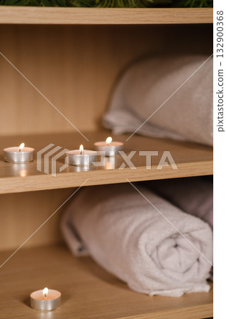 Soft towels and candles arranged on wooden shelf in spa setting, creating a calming atmosphere for relaxation and self-care during spa day enjoyment 132900368