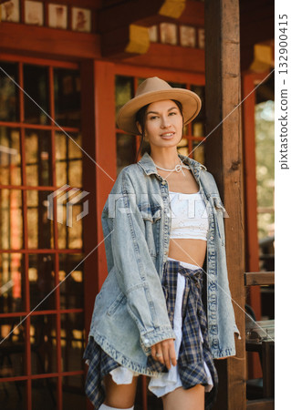 Young woman in stylish outfit stands near wooden structure in outdoor setting during sunny day Young woman in stylish outfit stands near wooden structure in outdoor setting during sunny day 132900415