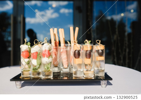 Unique appetizer display featuring elegant small glasses filled with fresh ingredients and flavors at a sunny outdoor event in the afternoon 132900525