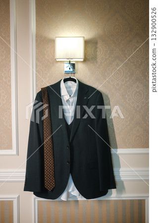Formal suit hanging in a hotel room with a tie draped across the shoulder in soft ambient lighting 132900526