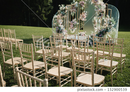 Chairs arranged in a beautiful outdoor setting for a wedding ceremony surrounded by greenery and floral decorations 132900539