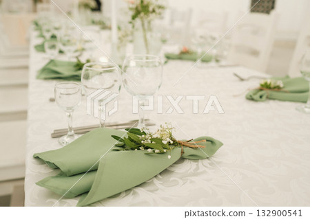 Elegant dining setup with green napkins and glassware at a decorated table for a special event in a bright venue Elegant dining setup with green napkins and glassware at a decorated table for a special event in a bright venue 132900541