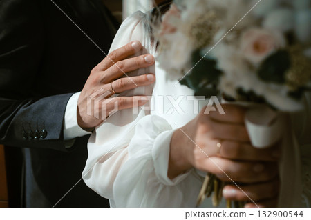 Couple sharing a romantic moment, showcasing wedding rings and bouquet in a soft-lit indoor setting during their wedding ceremony Couple sharing a romantic moment, showcasing wedding rings and bouquet in a soft-lit indoor setting during their wedding ceremony 132900544