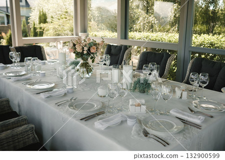 Elegant outdoor dining setup with floral arrangements and glassware on a sunny afternoon Elegant outdoor dining setup with floral arrangements and glassware on a sunny afternoon 132900599