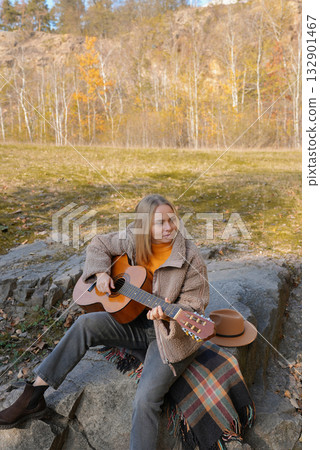 Portrait of smiling caucasian artist plays wooden acoustic guitar in autumnal park. Young songwriter plays string musical instrument hobby outside in nature fall time. Audio music healing 132901467