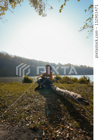 Blonde woman playing string guitar outdoors in autumn forest. Concept of sound therapy, mental health and wellness rituals. Calmness tranquility audio-sensory practices. Aura farming energy 132901471