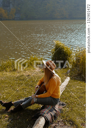 Beautiful blonde girl playing acoustic guitar and singing relaxing enjoying outdoors on sunny autumn day. Hippie woman in boho style learning and practicing playing musical instrument. Fall leaves Beautiful blonde girl playing acoustic guitar and singing relaxing enjoying outdoors on sunny autumn day. Hippie woman in boho style learning and practicing playing musical instrument. Fall leaves 132901472