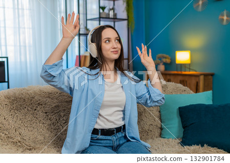 Young woman wearing wireless headphones on sofa dancing smiling happily enjoying favorite song 132901784