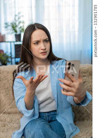 Young woman on sofa irritated arguing emotionally over video call waving hand conflict stress 132901785
