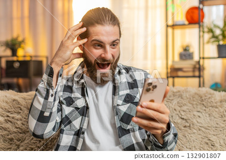 Young man typing fast at home, smartphone deal hunt, excitement, sudden wow, big online find 132901807