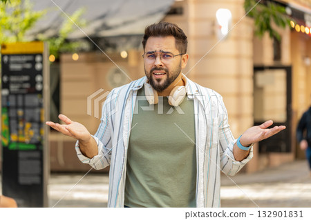Doubtful sad frustrated young Caucasian man shrugging shoulders dont know answer on city street 132901831