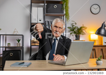 Senior businessman working on laptop showing thumb down gesture expressing bad work at home office 132901869