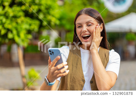 Happy Caucasian young woman using smartphone celebrating win good message news on city town street Happy Caucasian young woman using smartphone celebrating win good message news on city town street 132901878