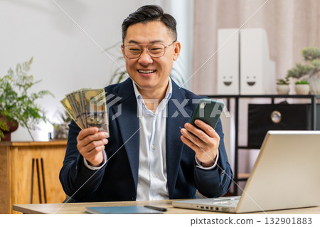 Happy rich Asian businessman counting money cash use smartphone app earning profit success contract Happy rich Asian businessman counting money cash use smartphone app earning profit success contract 132901883