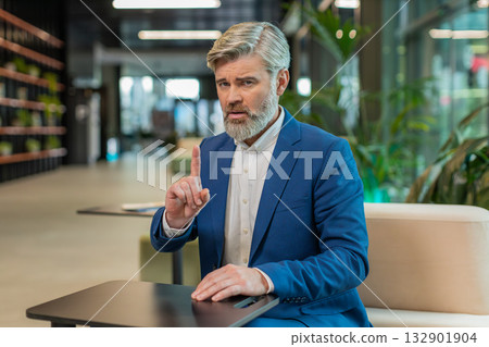 Serious mature businessman shakes finger and saying No be careful and giving advice in office lobby 132901904