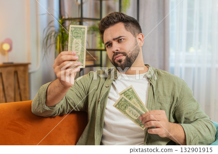 Poor Caucasian young man upset over insufficient amount of money, counting dollar banknotes at home 132901915