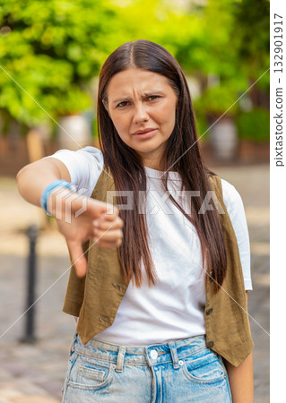 Upset young Caucasian woman lady showing double thumbs down expressing discontent on city street 132901917