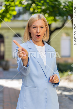 Caucasian mature businesswoman in suit standing in city street looking at camera shaking finger Caucasian mature businesswoman in suit standing in city street looking at camera shaking finger 132902016