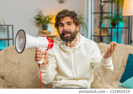 Young man in hoodie shout in megaphone loudspeaker announces discounts sale at home apartment 132902019